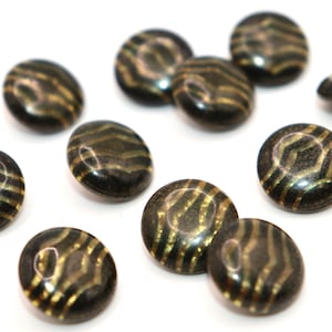 Puede incluir: Un conjunto de botones redondos, marrón oscuro, con acabado brillante. Cada botón presenta un patrón dorado en forma de onda. Los botones están dispersos sobre un fondo blanco, resaltando su diseño. Ideales para proyectos de costura.
