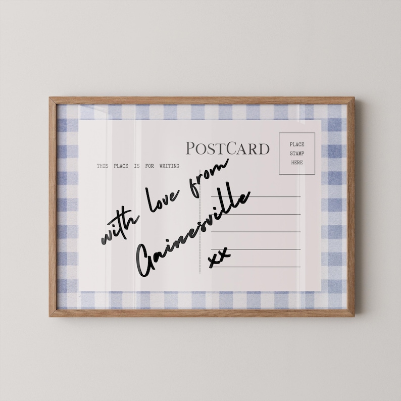 Pode incluir: Uma impress&atilde;o emoldurada de cart&atilde;o postal com uma borda de padr&atilde;o xadrez vichy azul claro e branco. O cart&atilde;o postal diz "with love from Gainesville" em escrita preta. A moldura &eacute; de madeira marrom clara.