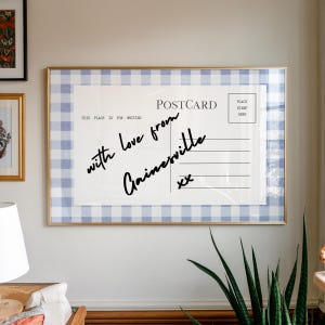 Pode incluir: Uma impress&atilde;o emoldurada de cart&atilde;o postal com uma borda xadrez azul e branca. O cart&atilde;o postal diz "with love from Gainesville" em escrita manuscrita. A moldura &eacute; dourada.