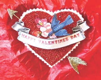 May include: A red glitter heart with a white banner that says "Happy Valentines Day". A blue bird with a white flower is on the heart.