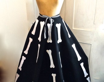 May include: A black skirt with a white bone print, displayed on a mannequin. The skirt has a flared silhouette and a striped tie at the waist. The design is a unique, eye-catching style.