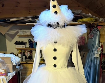 May include: A white clown costume with a cone hat, a ruffled collar, and a long-sleeved bodice. The hat has black polka dots. The bodice has three black buttons. The skirt is made of tulle.