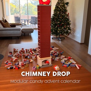 May include: A tall, red, brick-patterned chimney advent calendar with Santa's legs protruding from the top and a fireplace base. The text CHIMNEY DROP Modular candy advent calendar is displayed. Scattered around the base are various wrapped candies.