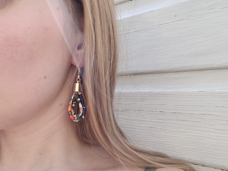 May include: A pair of dangle earrings with a gold accent. The earrings are made of fabric with a floral pattern in shades of orange, blue, and green.