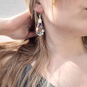 May include: A pair of silver hoop earrings with a colorful fabric design. The fabric is a mix of red, blue, green, and white.