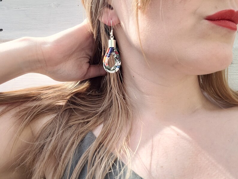 May include: A pair of silver hoop earrings with a colorful fabric design. The fabric is a mix of red, blue, green, and white.