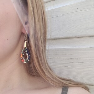 May include: A pair of dangle earrings with a gold top and a fabric loop. The fabric is a mix of orange, green, and black with a floral pattern.
