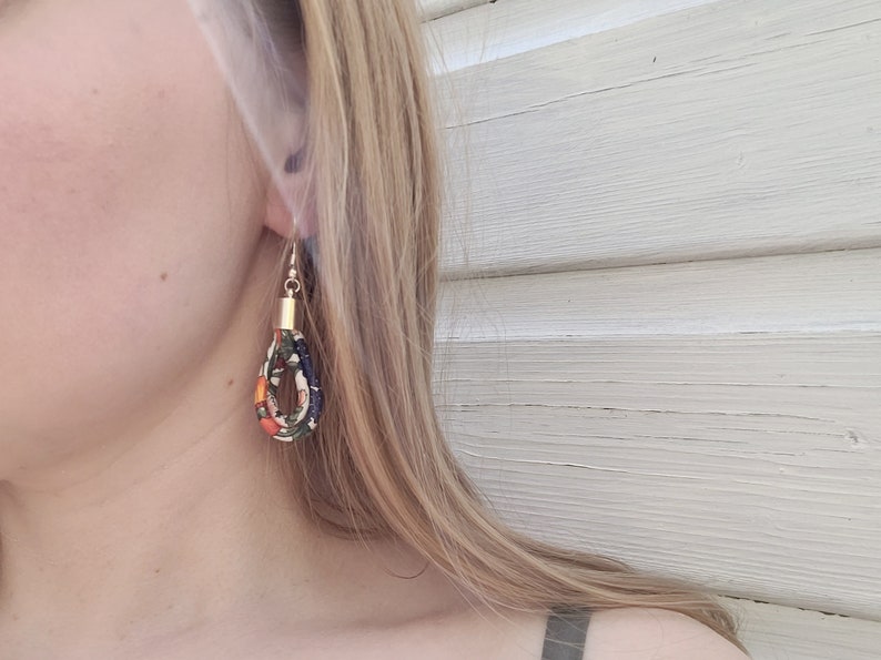 May include: A pair of dangle earrings with a gold top and a fabric loop. The fabric is a mix of orange, green, and black with a floral pattern.