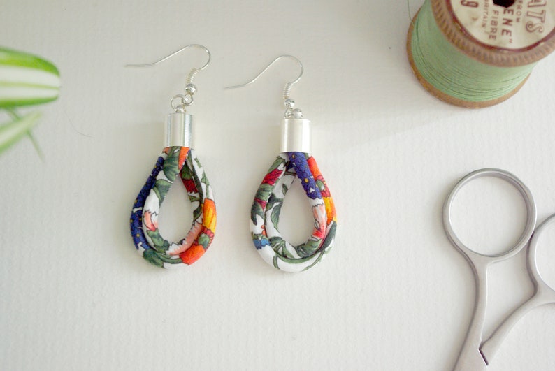 May include: Two pairs of floral fabric earrings with silver hooks. The fabric is white with orange, blue, and green floral patterns.