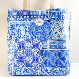Könnte beinhalten: Eine blau-weiße Tragetasche mit Patchwork-Design. Die Tasche hat eine Vielzahl von geometrischen und floralen Mustern in Blautönen mit cremefarbenen Griffen. Der Text "bunny bosworth" ist sichtbar.