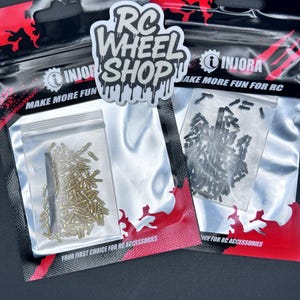 Può includere: Due sacchetti di plastica trasparente contenenti piccole parti metalliche, probabilmente per veicoli RC. I sacchetti sono sigillati in un imballaggio nero e rosso. Il testo "RC WHEEL SHOP" e "INJORA" sono visibili, insieme alla frase "MAKE MORE FUN FOR RC".