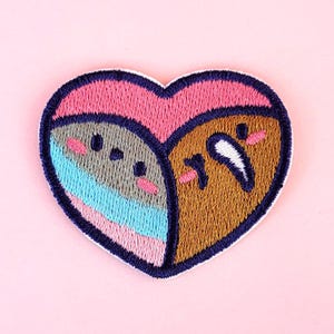 Op de afbeelding: Geborduurde strijkpatch in de vorm van een hart met twee cartoon gezichten erin. De gezichten zijn bruin, grijs, roze en blauw.