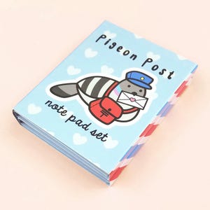 Puede incluir: Un juego de blocs de notas azul y blanco con una paloma de dibujos animados que lleva un sombrero y lleva una carta. La portada dice "Pigeon Post note pad set".