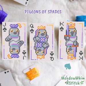 May include: Three cross-stitch patterns on fabric featuring playing cards with pigeon illustrations. The cards are labeled J, Q, and K with spade symbols. The text PIGEONS OF SPADES is centered above. The designs use purple, orange, and gray thread.