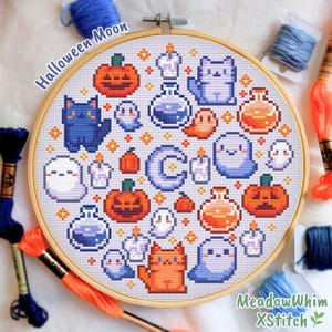 Può includere: Un telaio da ricamo rotondo in legno contenente un motivo a punto croce con elementi pixelati di Halloween, tra cui zucche arancioni, gatti blu e arancioni, fantasmi bianchi, pozioni viola, candele e una luna crescente blu centrale.