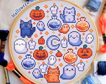 May include: A round wooden embroidery hoop containing a cross-stitch pattern featuring pixelated Halloween motifs including orange pumpkins, blue and orange cats, white ghosts, purple potion bottles, candles, and a central blue crescent moon.