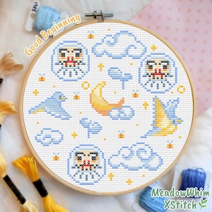 May include: A cross-stitch embroidery hoop with a charming design of a blue bird, clouds, a crescent moon, and stars. The design includes the text "Good Beginning" and "MeadowWhim XStitch". The embroidery is set in a wooden hoop.