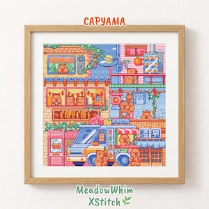 Op de afbeelding: Een ingelijst kruissteekpatroon getiteld CAPYAMA met een levendige pixel-art scène van capibara's in een stad. Het ontwerp bevat een café, een foodtruck en diverse capibara's in ramen en winkels met kleurrijke details en tekst.