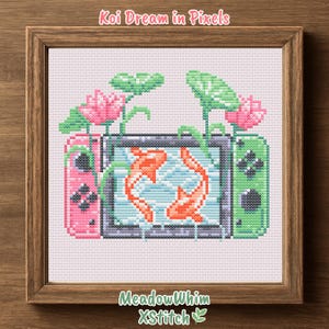 May include: Cross-stitch art in a wooden frame. The design features a pixelated koi fish swimming in a pond, framed by a pink and green game console. Pink lotus flowers and green lily pads are also included. Text at the top says "Koi Dream in Pixels".