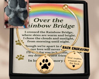 May include: A gold-colored bracelet with two round charms, one featuring a paw print and the name "Muffin", the other with a heart and space for a custom message. The text "Over the Rainbow Bridge" is visible.