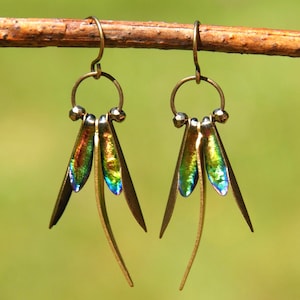 May include: A pair of dangle earrings featuring bronze-toned metal hooks and circular connectors. Each earring displays three slender, pointed petals with a vibrant, iridescent finish in shades of green, blue, and gold, suspended from the metal ring.