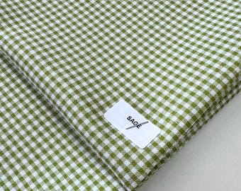 May include: Close-up of a sage green and white gingham fabric. The fabric is folded, revealing a pattern of small, evenly spaced squares. A white label with the word "SAGE" is attached to the fabric.