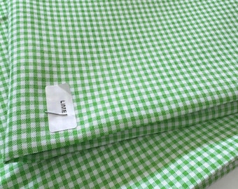 May include: Close-up of folded lime green and white gingham fabric. The fabric has a classic checkered pattern. A tag with the word "LIME" is attached to the fabric.