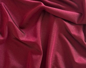 May include: Close-up of a deep burgundy fabric with a subtle sheen. The material is draped, creating soft folds and shadows. The texture appears smooth and possibly silky, suggesting a luxurious textile.