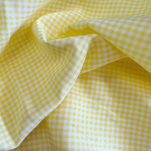 May include: Close-up of a yellow and white gingham fabric. The fabric is folded and draped, showing the texture and pattern of the woven material. The yellow squares are bright and the white squares are crisp.