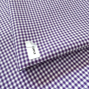 May include: Close-up of a purple and white gingham fabric. The fabric is folded, revealing a tag that reads "PURPLE". The checkered pattern is made up of small, evenly spaced squares.