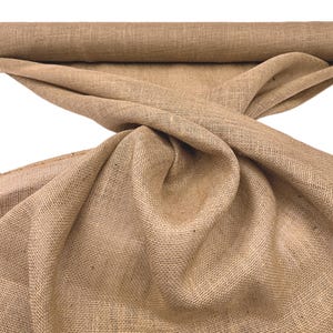 May include: A roll of natural burlap fabric, with a coarse, woven texture. The fabric is a warm, earthy brown color, and is partially unrolled, with folds and creases visible. The background is plain white.