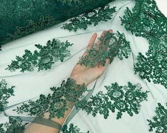 May include: A roll of emerald green lace fabric with floral embroidery. The fabric is a sheer mesh with detailed, raised floral patterns and small sequins. The lace is displayed on a white surface.