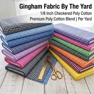 May include: A collection of folded gingham fabric bolts in various colors including black, blue, pink, green, orange, and yellow. The fabric features a 1/8 inch checkered pattern. A gold metal ruler and gold scissors are placed on the fabric.