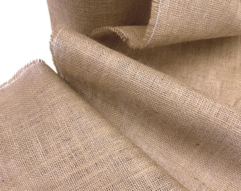 May include: Close-up of a roll of natural burlap fabric. The fabric is a light brown color with a coarse, woven texture. The edges are frayed, with a white thread visible along the border. The burlap is rolled and folded, showing its thickness and flexibility.