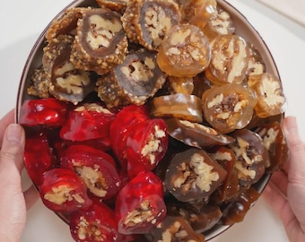 May include: A bowl of traditional sweets, including walnut-filled rolls with a brown coating, translucent amber pieces, and bright red, jelly-like candies. The bowl is held by hands. The image shows a variety of textures and colours.