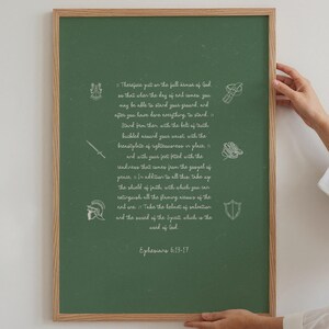 Puede incluir: Una impresión enmarcada con un fondo verde y texto blanco de Efesios 6:13-17. El texto está acompañado de pequeñas ilustraciones blancas de un escudo, una espada, un casco y otros símbolos. El marco es de color marrón claro.