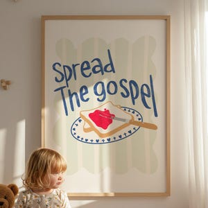 Puede incluir: Un estampado enmarcado con las palabras "Spread The Gospel" sobre un gráfico de tostadas con mermelada. Un niño con un mono floral está sentado en un banco junto a un oso de peluche, un juguete apilable de madera y una manta doblada.