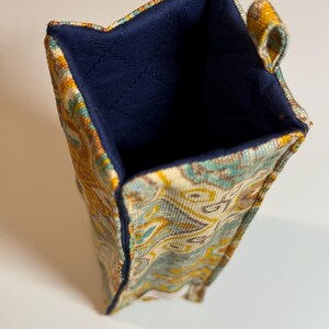 May include: A rectangular fabric container with a colorful paisley pattern in shades of yellow, teal, and cream. The interior is a solid navy blue, and the edges are neatly stitched. A small loop is attached to the side.
