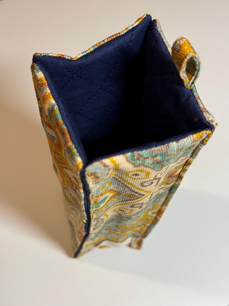 May include: A rectangular fabric container with a colorful paisley pattern in shades of yellow, teal, and cream. The interior is a solid navy blue, and the edges are neatly stitched. A small loop is attached to the side.