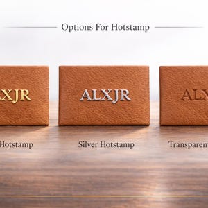 May include: Three brown leather boxes with the letters "ALXJR" hot stamped in gold, silver, and transparent. The text "Options For Hotstamp" is above the boxes. The boxes are on a wooden surface.