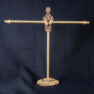 May include: An antique-style gold towel rack. It has a decorative base, a twisted central pole, and two horizontal bars with decorative ends. The central section features cherub figures. The rack's design is ornate and vintage, suitable for a bathroom.