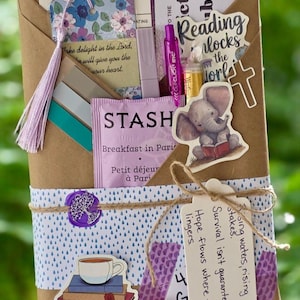 May include: A brown paper-wrapped gift set with a floral bookmark, tea, pen, and stickers. The set includes a reading list, a sticker of an elephant reading a book, and a tag with inspirational text. The set is tied with twine.