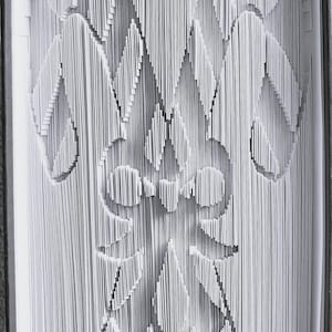 Op de afbeelding: Een uniek boekkunstwerk met een zuurstok- en strikdesign uitgesneden in de pagina's. De monochrome afbeelding toont de ingewikkelde details van het gevouwen papier en creëert een feestelijk vakantiethema.