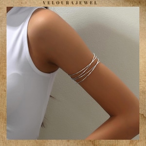 Op de afbeelding: Zilveren armmanchet met een multi-strand ontwerp. De sieraden worden op de bovenarm gedragen en zijn gemaakt van dun, getextureerd metaal. De afbeelding bevat ook de tekst "VELOURAJEWEL".