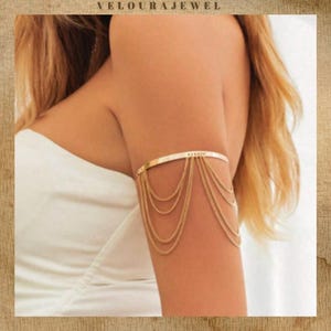 May include: Gold arm cuff with cascading chain strands. The upper arm jewellery has a simple, elegant design. The accessory is a stylish piece of jewellery.