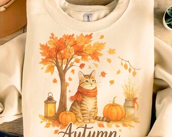 May include: Cream-colored sweatshirt featuring an autumn-themed graphic. The design includes a tabby cat wearing a scarf, pumpkins, a tree with orange leaves, and the word "Autumn". The sweatshirt is a cozy fall-themed apparel item.