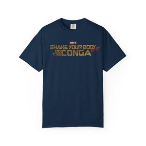 May include: Navy blue t-shirt with gold and red text that reads "Shake Your Body Do The Conga Baby". The shirt has a crew neck and short sleeves. The text is in a bold, stylized font.