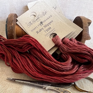 May include: A spool of red embroidery floss with a label that reads "The Great Art Simply Shaker Ruby Slipper 7100 Colorfast".