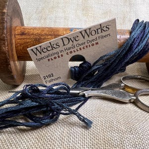 May include: A wooden spool with dark blue and purple embroidery floss, a Weeks Dye Works label, and silver scissors. The label reads "Weeks Dye Works" and "2102 Fathom". The floss is 6 yards.