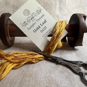 May include: A spool of gold embroidery floss with a label that reads "The Small Threads Sampler Gold Leaf 0420 COLORFAST".